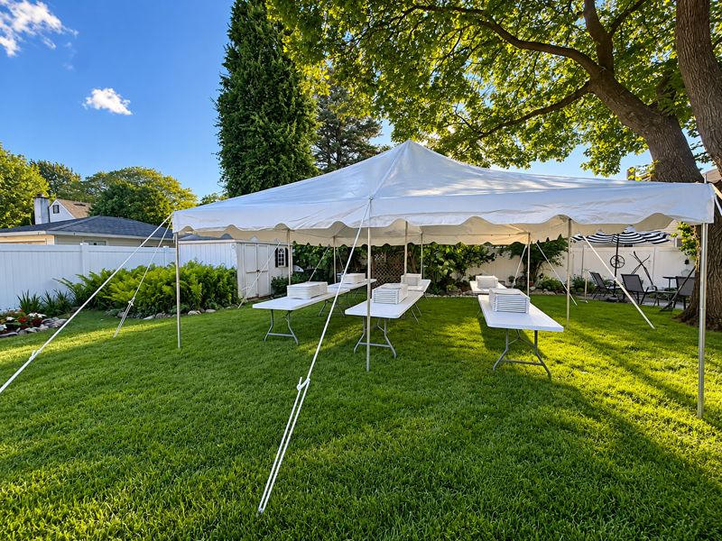 20 by 20 pole tent with banquet tables in a shaded backyard