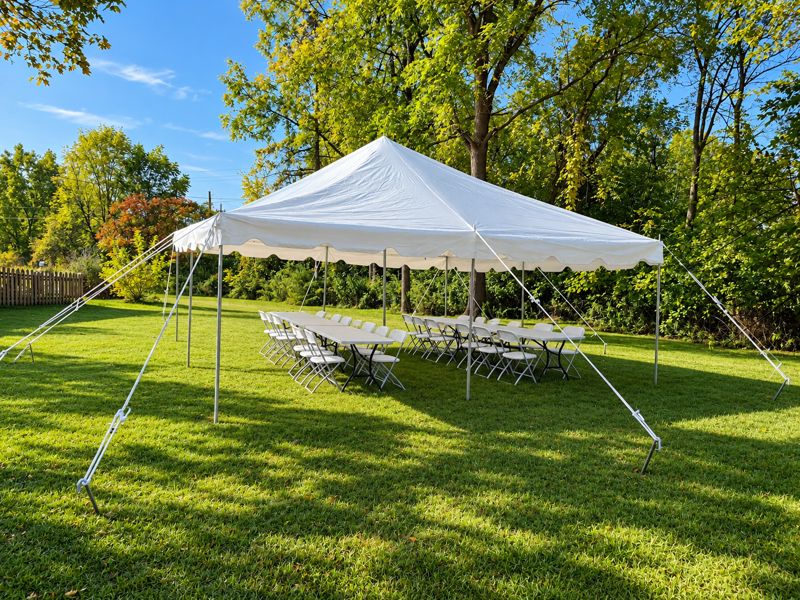 20 by 30 pole tent with long banquet tables and white chairs set for guests